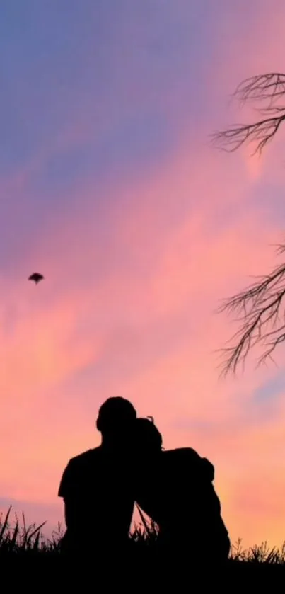 Couple silhouette against a pink sunset sky with tree branches.