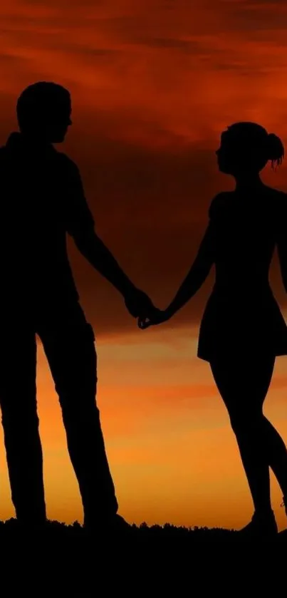 Silhouette of couple holding hands against an orange sunset sky.