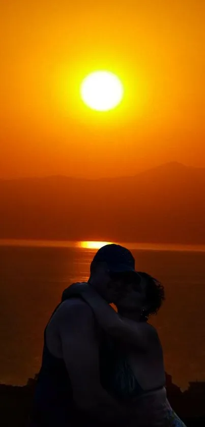 Romantic silhouette of a couple against an orange sunset over the ocean.