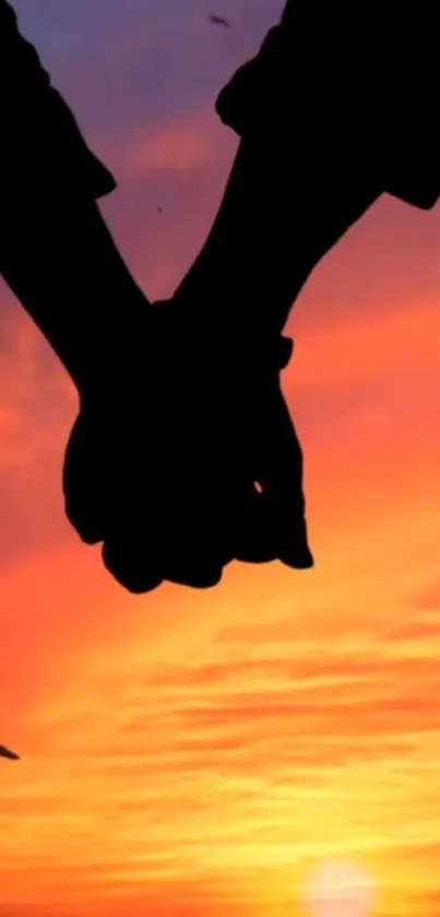 Silhouette of a couple holding hands against an orange sunset sky.