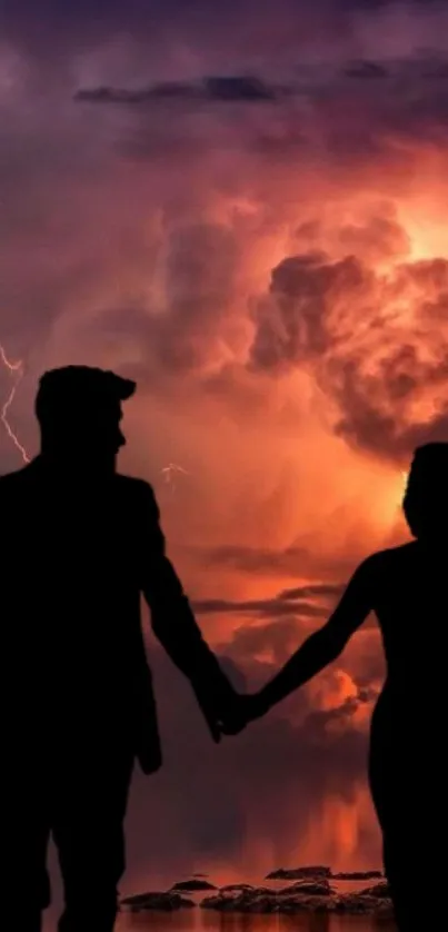 Silhouette of a couple holding hands against a dramatic sunset sky.