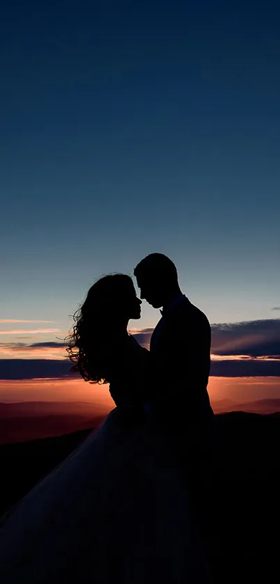 Silhouette of a couple embracing at sunset with a dark blue sky.