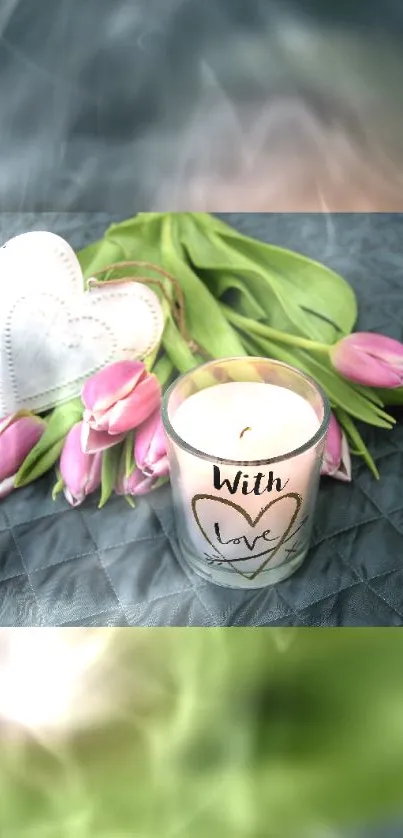 Candle with love surrounded by pink tulips on a gray surface.