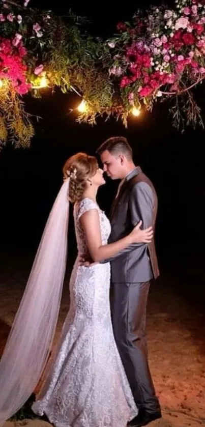 Wedding couple under floral arch at night.