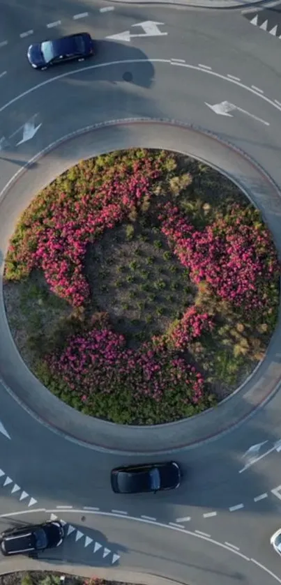 Aerial view of a roundabout with vibrant flowers and cars from above.