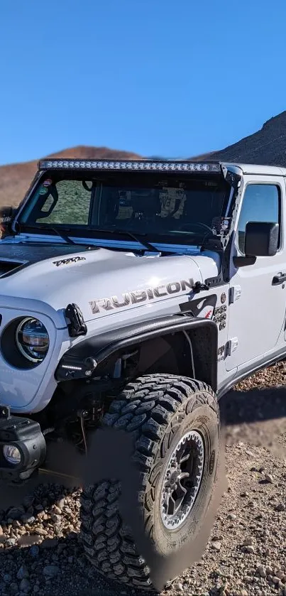 Off-road Jeep Rubicon on rocky terrain with mountain backdrop.