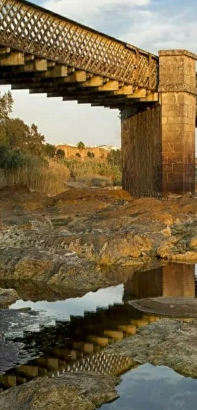 Rustic bridge over rocks with reflection under clear sky.