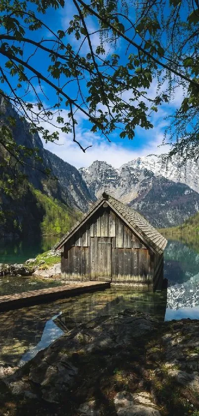 Rustic cabin by a serene mountain lake under blue skies.