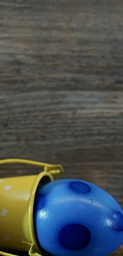 Yellow bucket with blue polka dot egg on wooden background.