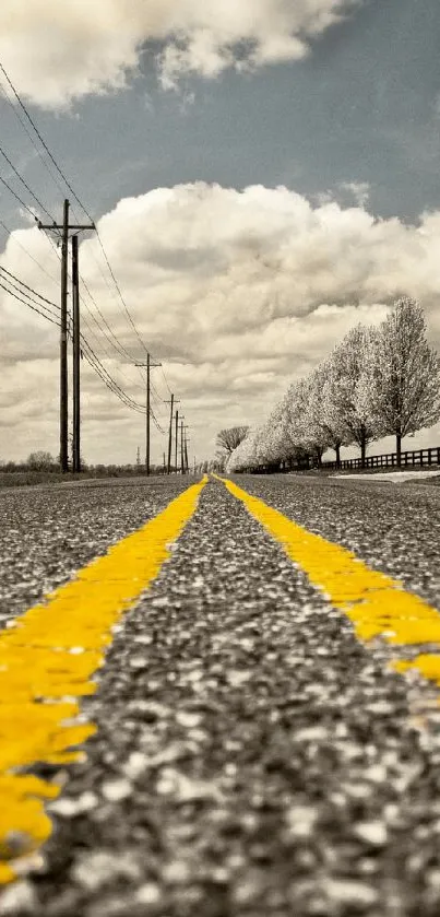 Rustic road with yellow lines under a cloudy sky, perfect for mobile wallpaper.