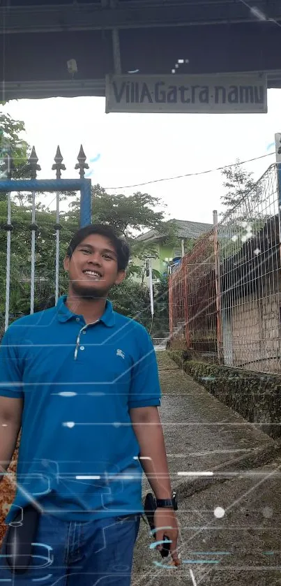 Man in blue shirt stands by a rustic villa entrance with green plants in the background.