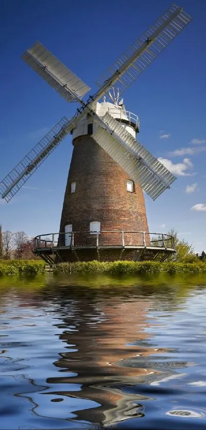 Rustic windmill reflecting in a calm lake under a clear blue sky.