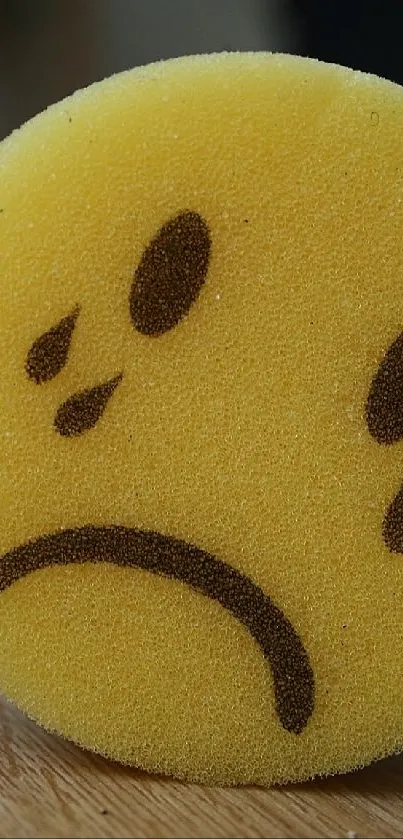 A sad emoji sponge on a wooden floor surface.