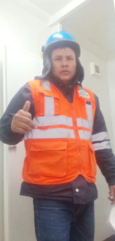 Construction worker in safety gear with orange vest and blue helmet in industrial setting.