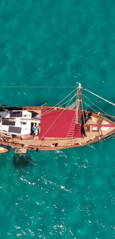 Aerial view of a sailing boat on vibrant turquoise ocean water.