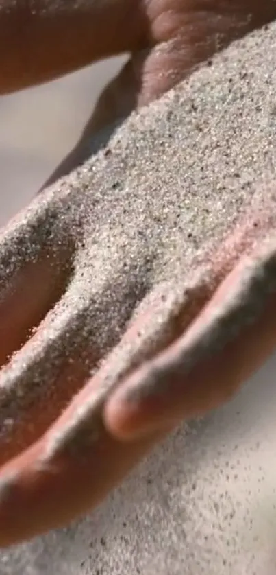 Close-up of sand flowing gently over a hand in a serene mobile wallpaper.