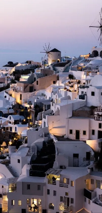 Stunning view of Santorini village at sunset with windmills and lit buildings.