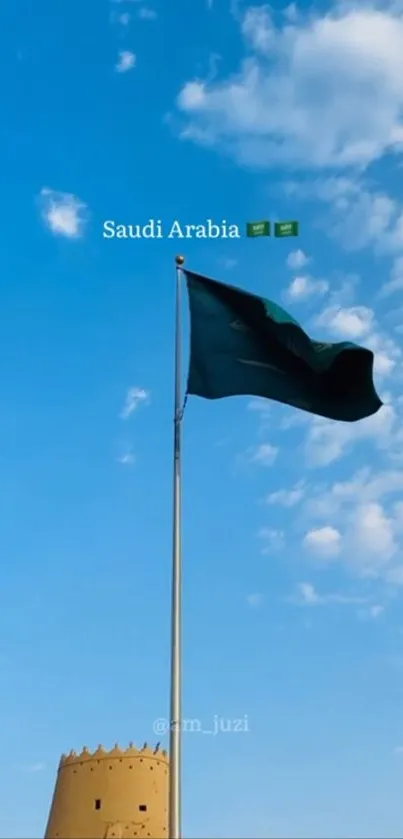 Saudi Arabia flag waves against a blue sky with cultural landmark in view.