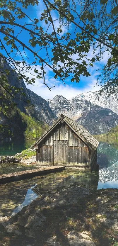 Rustic cabin by alpine lake and mountains under a blue sky.