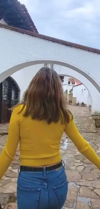 Stylish person walks through scenic white archway on a stone path.