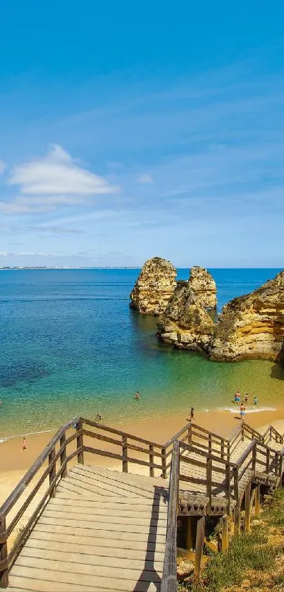 Wooden walkway leading to a scenic beach with blue ocean and rocky cliffs.