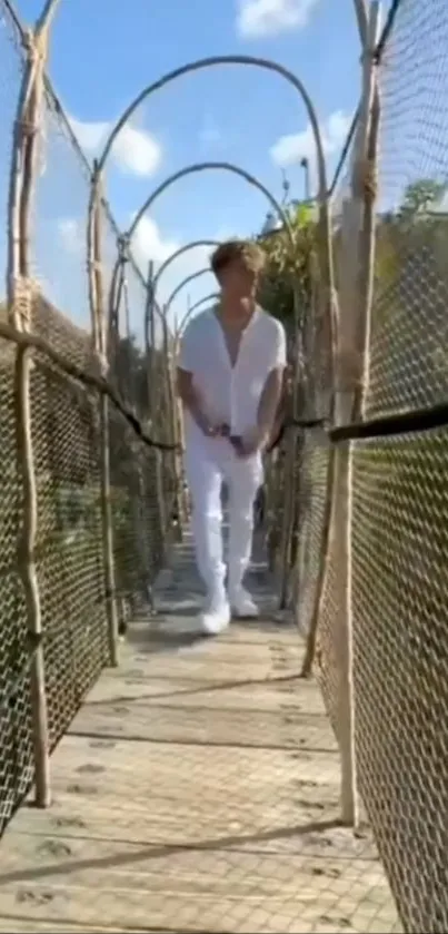 Man walking on a scenic bridge surrounded by greenery and clear blue sky.