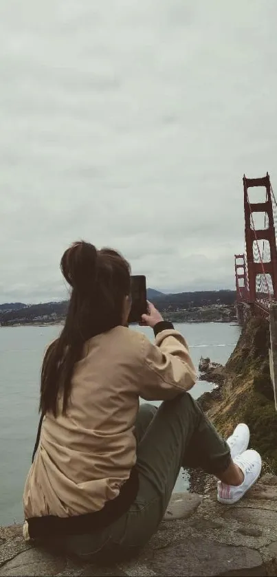 Woman photographing Golden Gate Bridge from a scenic viewpoint.