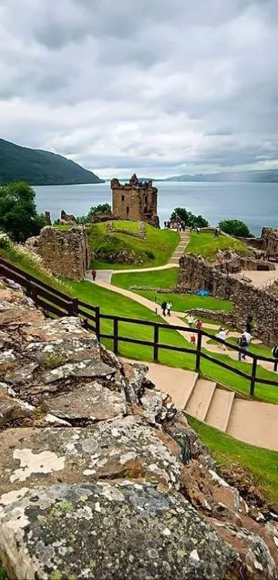 Scenic castle overlooking a lake with green hills and a cloudy sky.