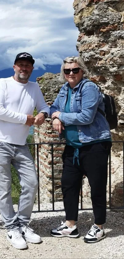 Two people pose by ancient ruins with a scenic backdrop.