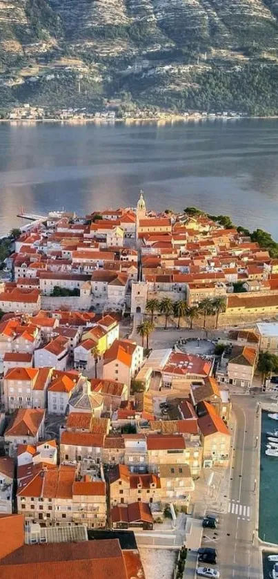 Aerial view of a coastal town with orange rooftops by the sea and mountains.