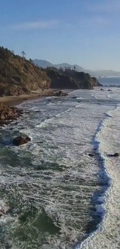 Aerial view of ocean waves crashing on a scenic rocky shoreline under a clear blue sky.