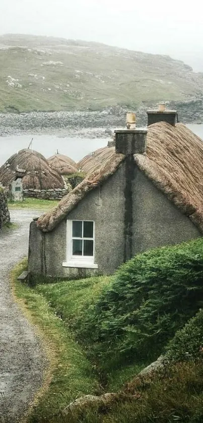 Cottage by a lake with greenery and a misty backdrop.