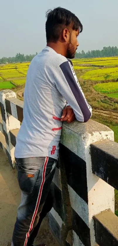 Man leaning on a bridge with scenic countryside fields.