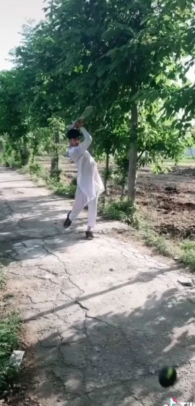 Person playing cricket on a green pathway under trees.