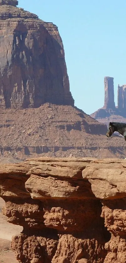 A lone rider on horseback overlooks a vast desert canyon under a clear blue sky.