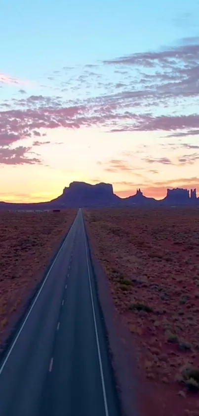 Desert highway at sunset with mountains and colorful sky.