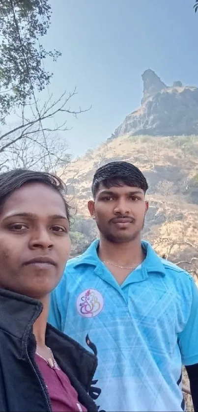 Two people pose with a scenic hilltop view in the background.