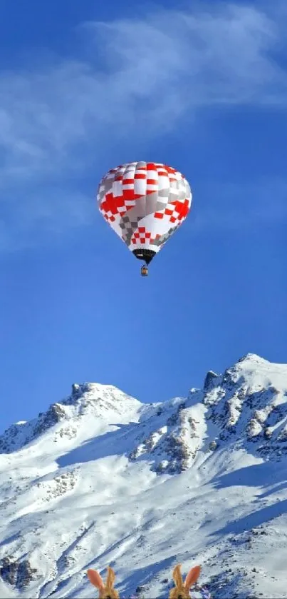 Hot air balloon over snowy mountains under blue sky.