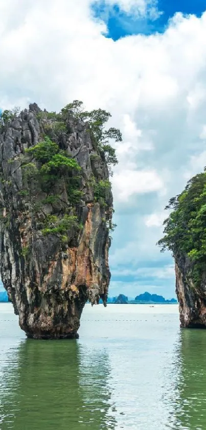 Tall rock island with lush greenery in tranquil ocean.