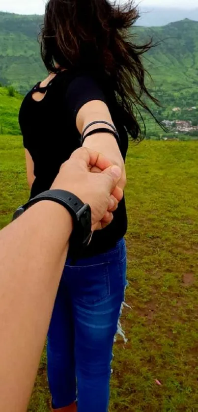 Couple holding hands in lush mountain landscape.