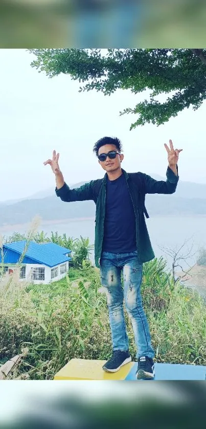 Man posing in front of a scenic lake view under a cloudy sky.