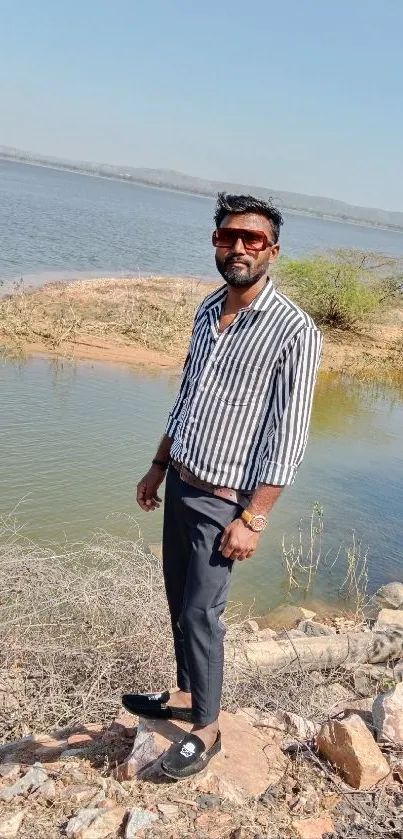 Man standing by a serene lake with clear blue water.