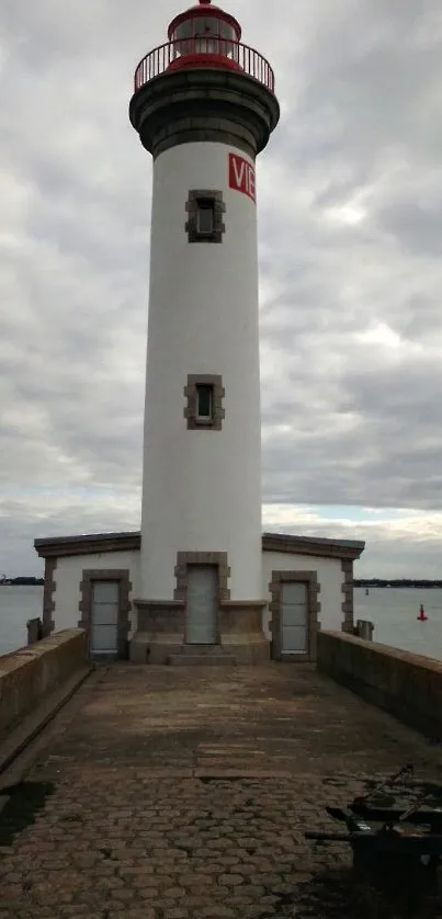 Lighthouse on a stone pathway by the ocean under a cloudy sky.