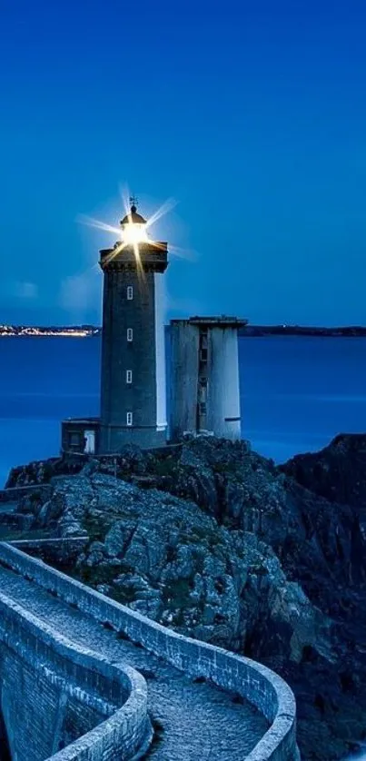 Lighthouse illuminated at night over a rocky ocean landscape.