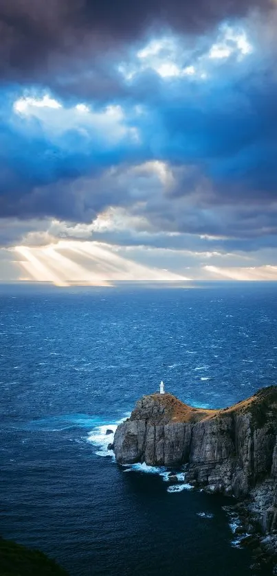 Lighthouse on cliff with ocean and beams of sunlight through clouds.