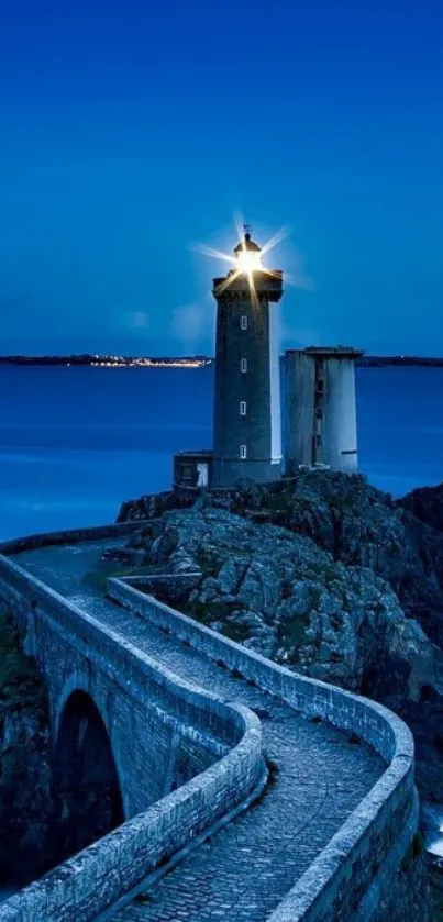 Lighthouse on rocky coast under deep blue sky at dusk.