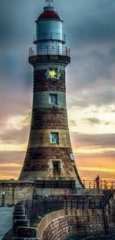 Sunset over a lighthouse by the ocean with a scenic sky.