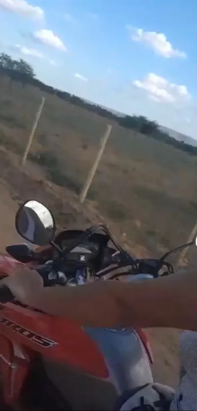 Person riding a motorcycle on a scenic country road under a blue sky.