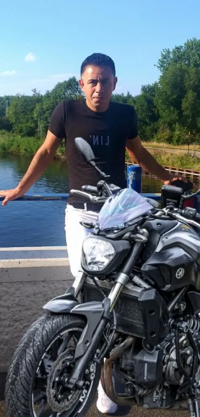 Man with motorcycle by a tranquil lakeside.