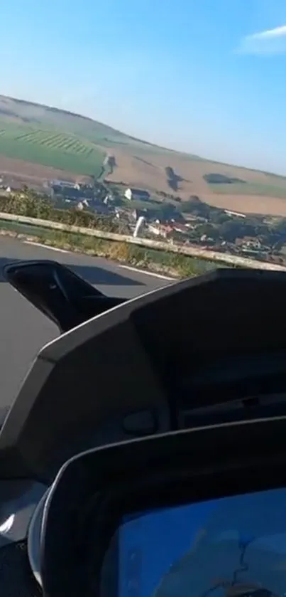 Motorcycle dashboard view with scenic landscape and clear blue sky.